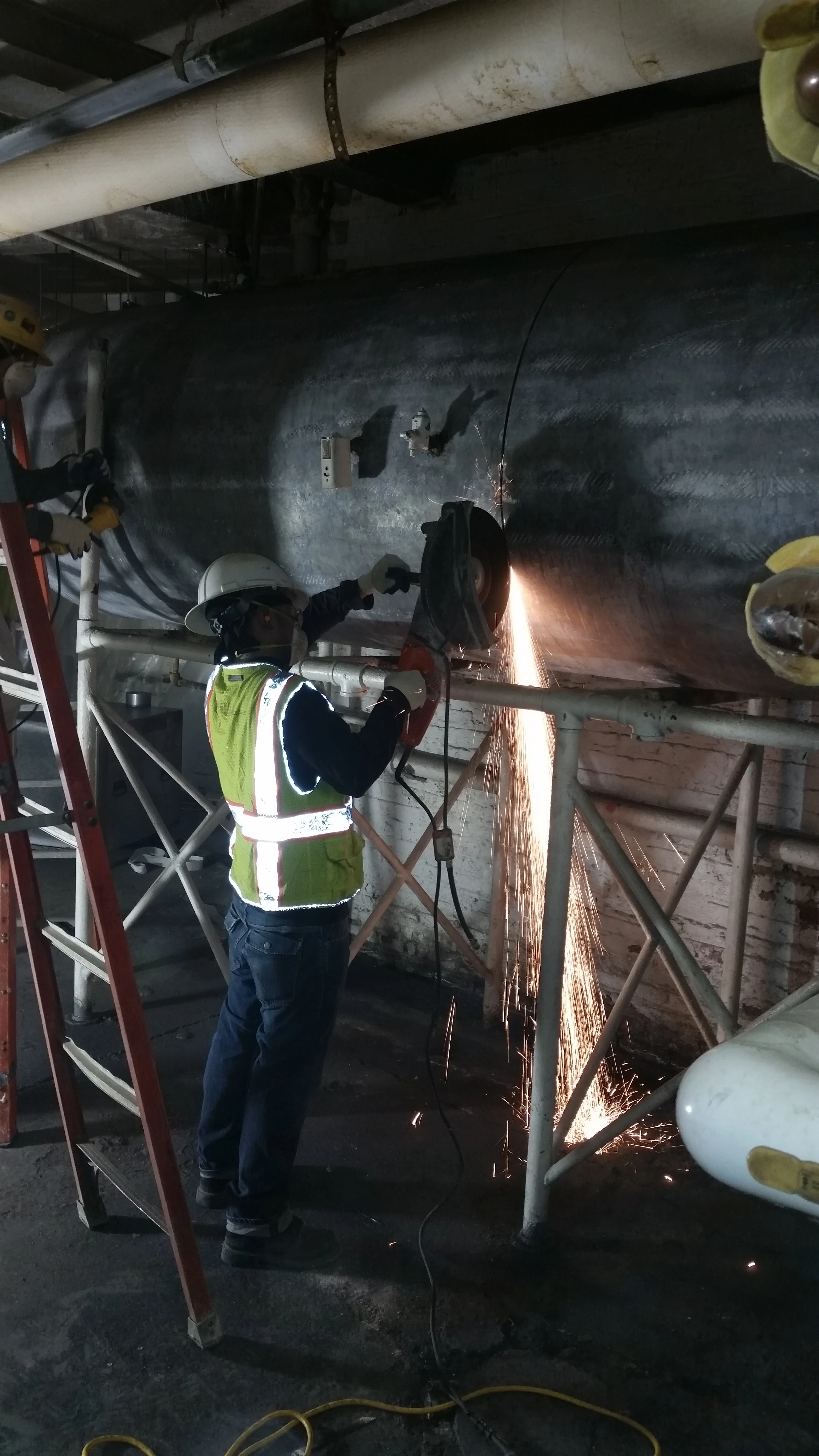 Worker in safety gear cutting industrial pipe with sparks flying in confined space