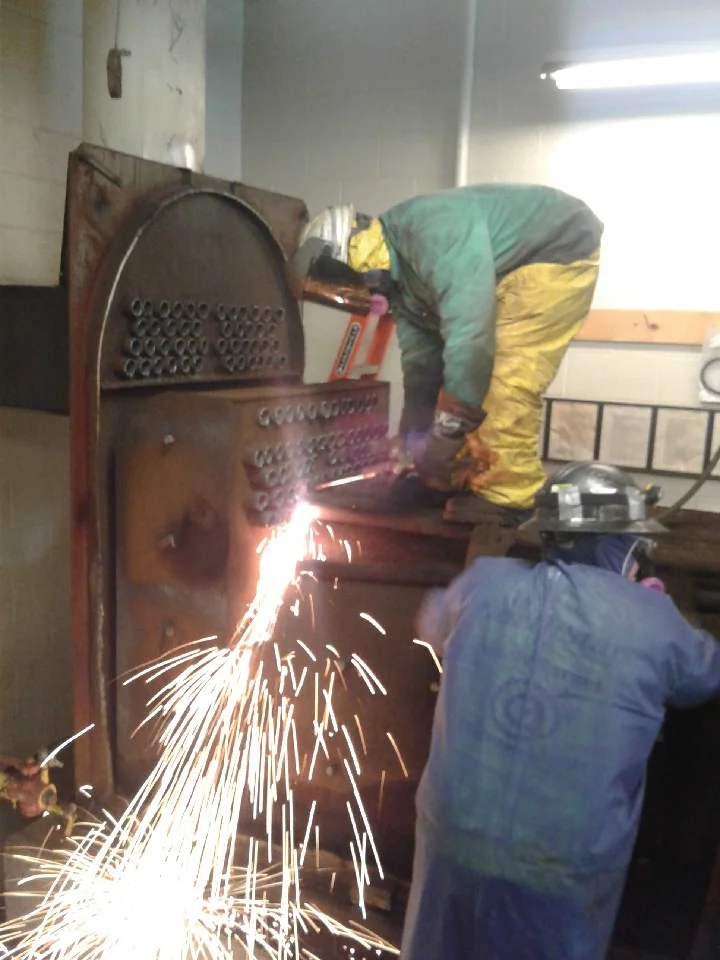 Worker using oxy-acetylene torch to cut industrial metal equipment during removal project