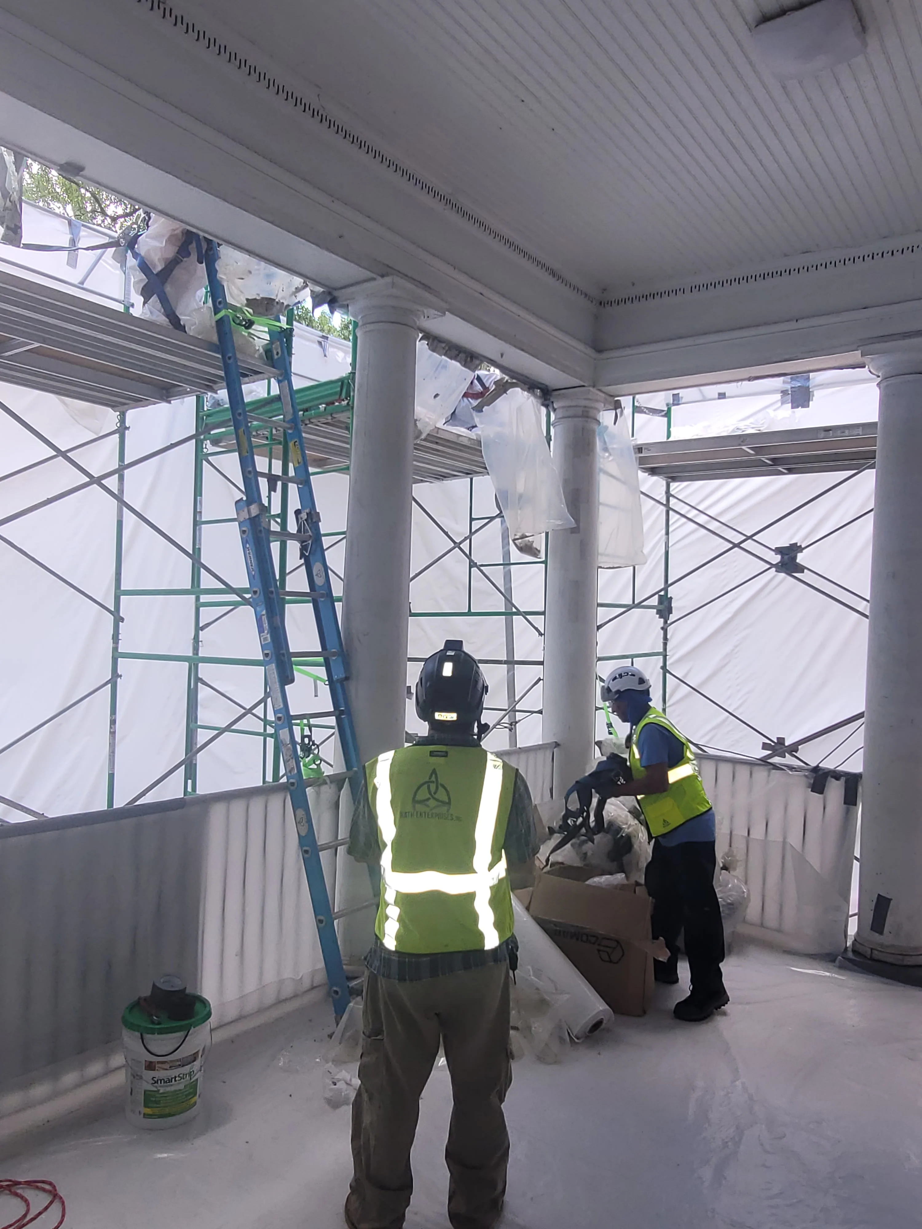 Asbestos removal crew in protective gear working in contained commercial space with metal walls